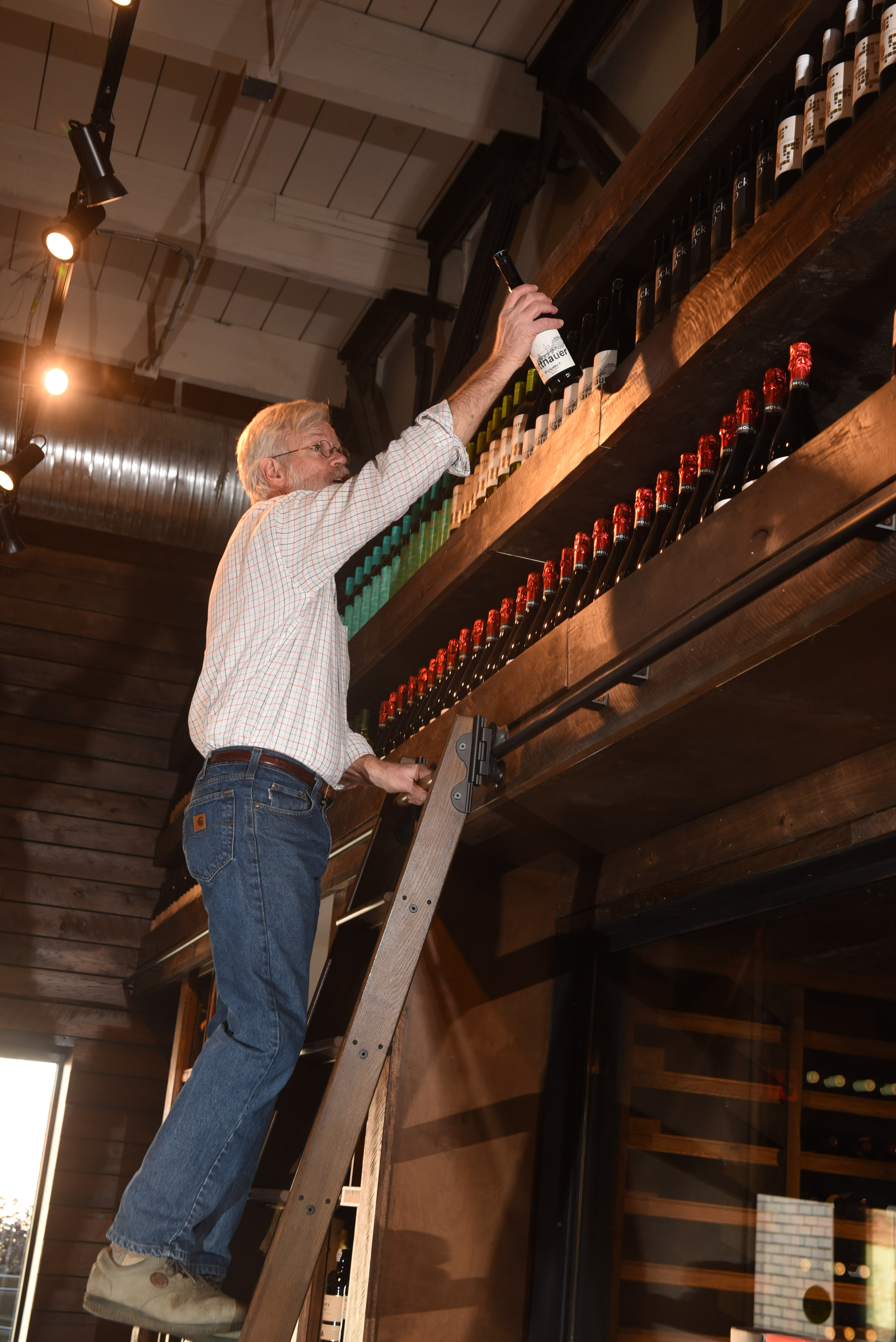 Brian Leutwiler puts away wine from a ladder inside the store, Imbibe, at 1616 Broad St.