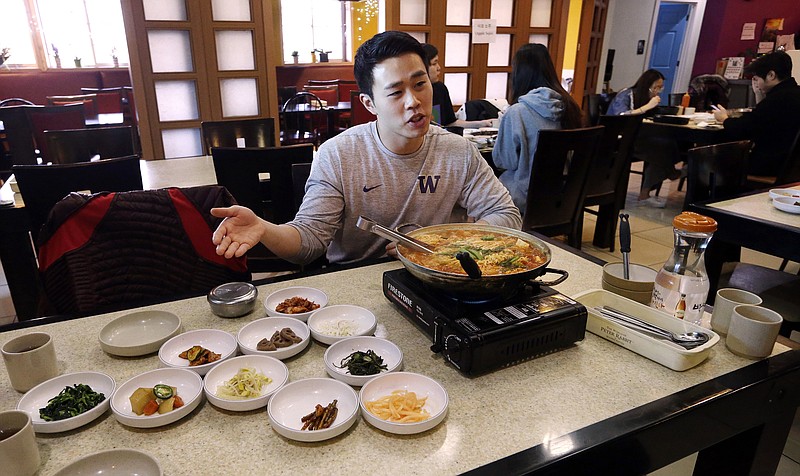 In this photo taken Dec. 12, 2017, server Young Kim talks about the South Korean dish called budae jjigae, or "army stew," he is serving simmering atop a heating plate at a Korean restaurant in Shoreline, Wash. SPAM, trout, fried chicken, moon pies and anything slathered in mayonnaise, those are some of the flavors of South Korea's home cooking that might seem just a bit familiar to the U.S. athletes and hordes of westerners preparing to descend upon the small Asian country for the 2018 Olympic Winter Games. (AP Photo/Elaine Thompson)