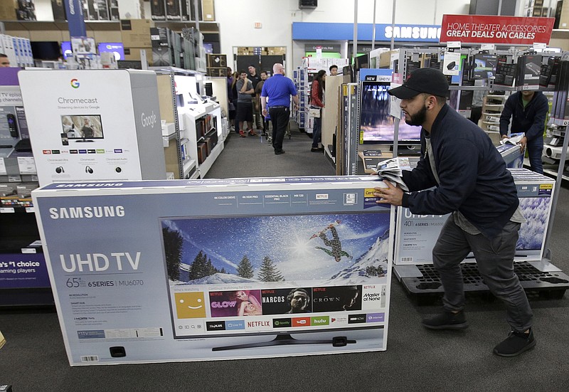 FILE - In this Nov. 23, 2017, file photo, Jesus Reyes pushes a television down an aisle as he shops at a Black Friday sale at a Best Buy store in Overland Park, Kan.