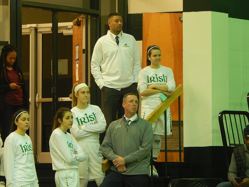 Notre Dame girls' basketball coach Jason Hill (lower right) and some of his players along with assistant coach De Lamb (above) watching some of the action before the Lady Irish played. It was Hill's birthday, but not a very happy one after his team's 53-14 loss.