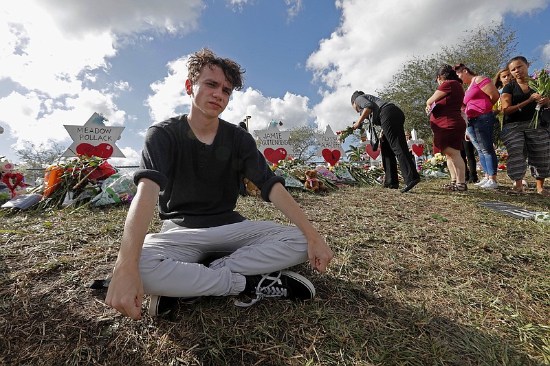 Chris Grady, a student at Marjory Stoneman Douglas High School, poses at a memorial outside the school, for Wednesday's mass shooting, in Parkland, Fla., Monday, Feb. 19, 2018. Grady huddled in his classroom at the high school last Wednesday listening to shots ring out nearby, what he felt wasn't fear, but anger. Grady and his friend are among about 100 Stoneman Douglas students who are heading to Florida's capital, Tallahassee, to push lawmakers to do something to stop gun violence. (AP Photo/Gerald Herbert)