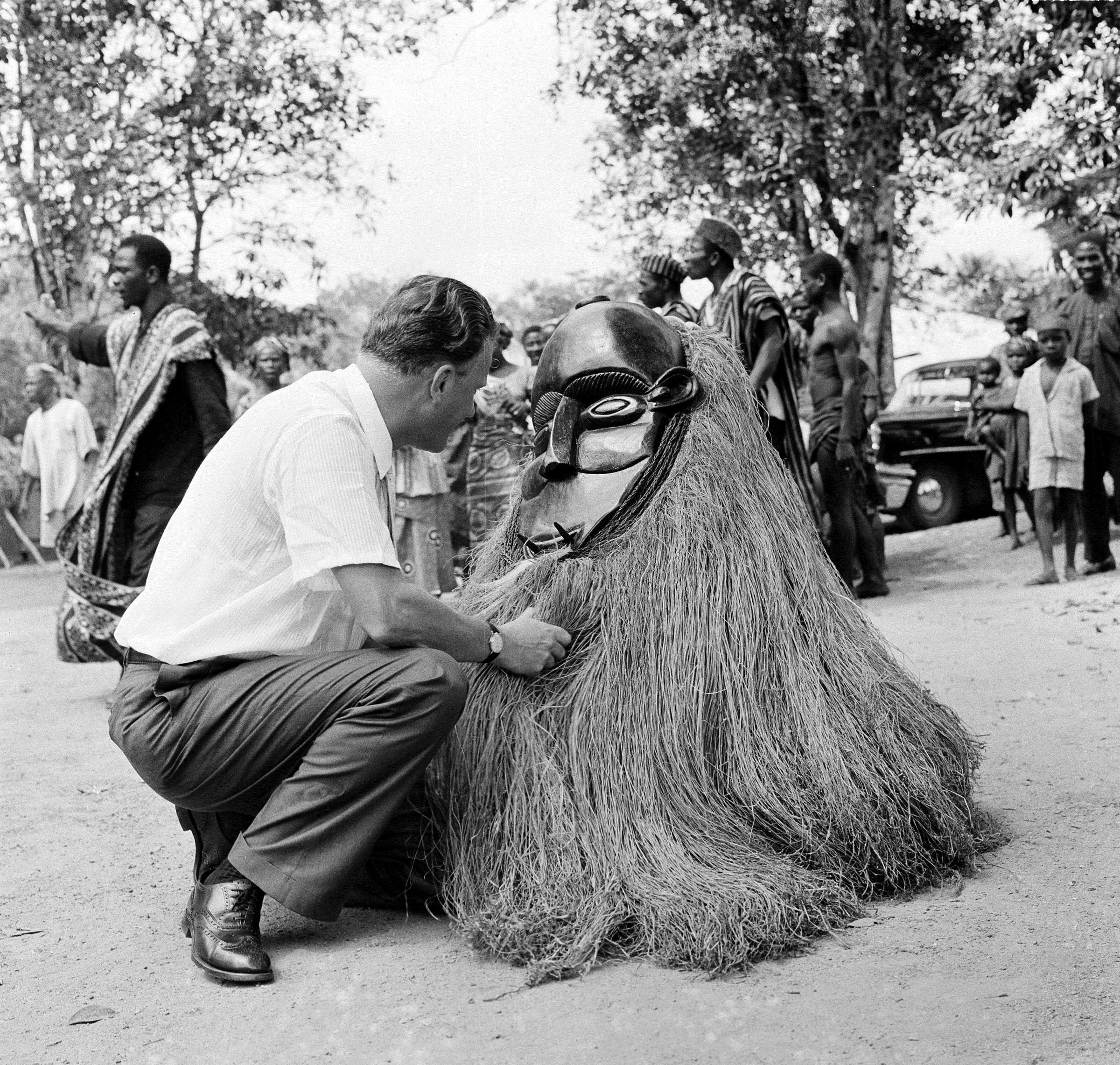 The Reverend Billy Graham kneels down to get a look at Liberian tribesman in the village of Bigwaakor, dressed in a costume representing an evil spirit, Jan. 28, 1960. (AP Photo