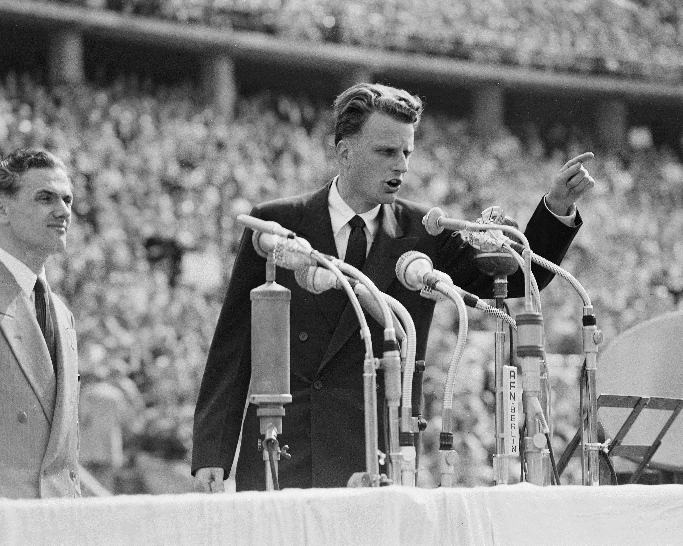 FILE - In this June 27, 1954 file photo, Evangelist Billy Graham speaks to over 100,000 Berliners at the Olympic Stadium in Berlin, Germany. Graham, who transformed American religious life through his preaching and activism, becoming a counselor to presidents and the most widely heard Christian evangelist in history, has died. Spokesman Mark DeMoss says Graham, who long suffered from cancer, pneumonia and other ailments, died at his home in North Carolina on Wednesday, Feb. 21, 2018. He was 99. (AP Photo, File)