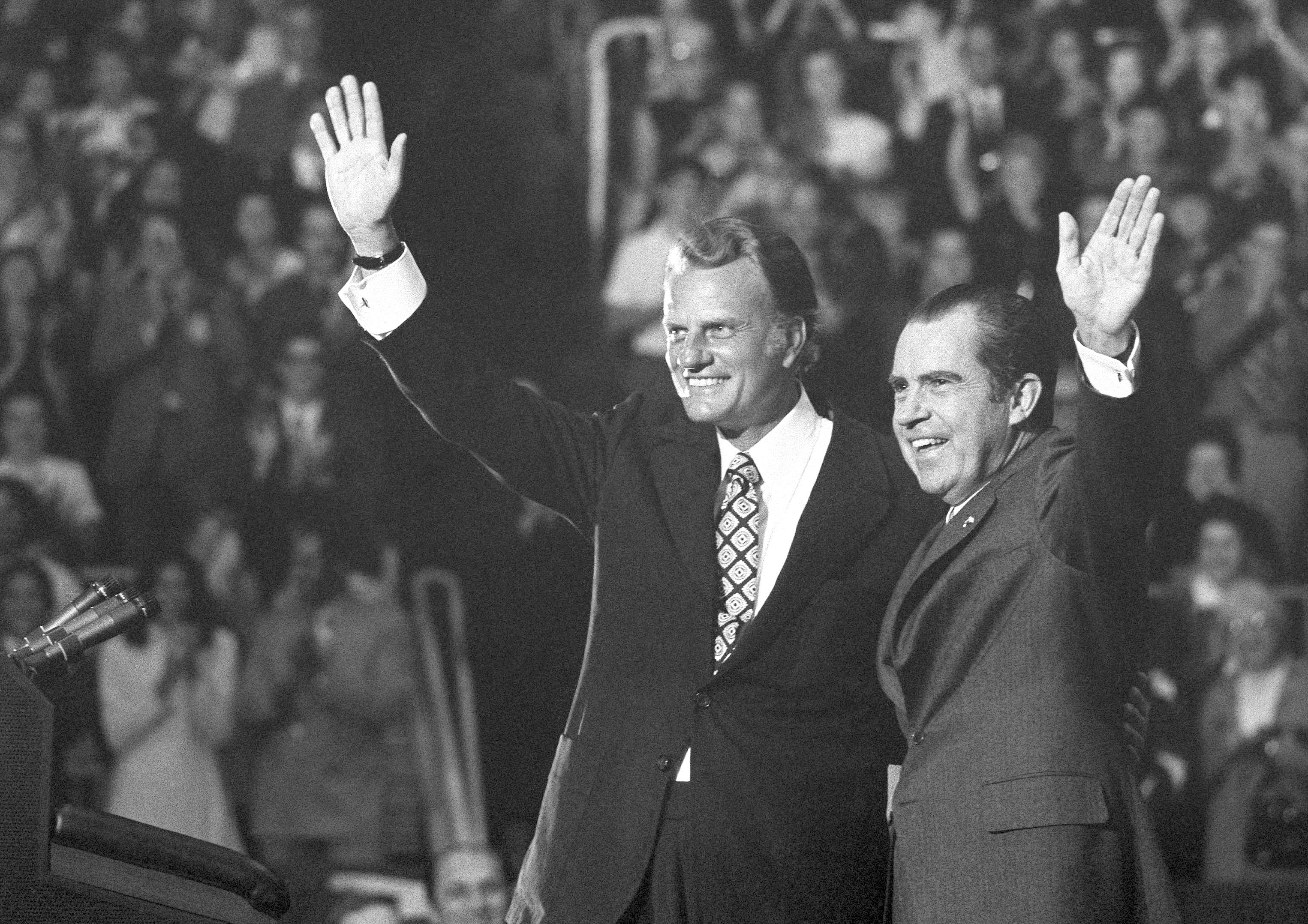 Evangelist Billy Graham and President Nixon wave to a crowd of 12,500 at ceremonies honoring Graham at Charlotte, North Carolina on Friday, Oct. 16, 1971. (AP Photo)