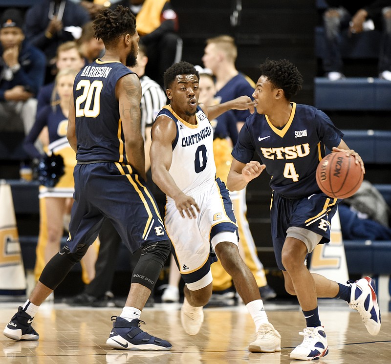 UTC's Makale Foreman, center, tries to get past the pick of ETSU's James Harrison, left, as Jason Williams works the ball around the perimeter during a game last month at McKenzie Arena. ETSU leads the SoCon standings entering the final regular-season weekend, but UNCG is just a game behind.