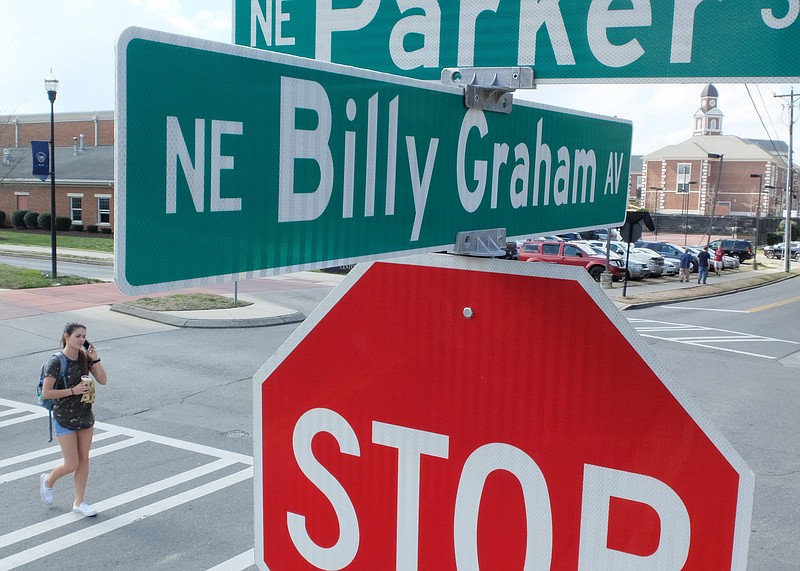 Lee University student Tiffany Sillamen crosses Billy Graham Ave, NE on the campus where the city is draping his street signs with black cloth and a white ribbon to honor "America's Pastor" Wednesday following his death at age 99. 