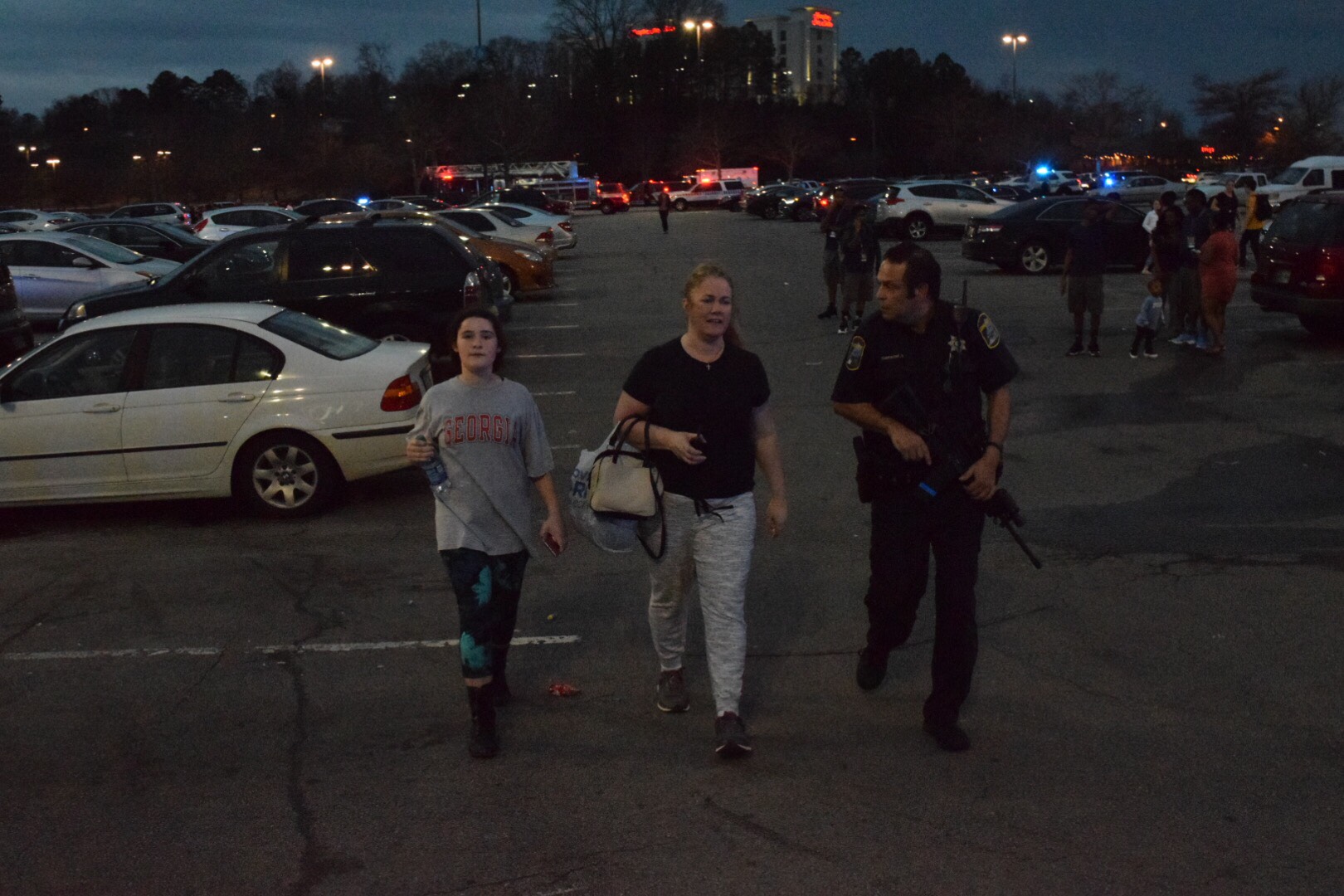People walk through the parking lot at Hamilton Place Mall with a police officer after reports of an active shooter on Saturday, Feb. 24, 2018.