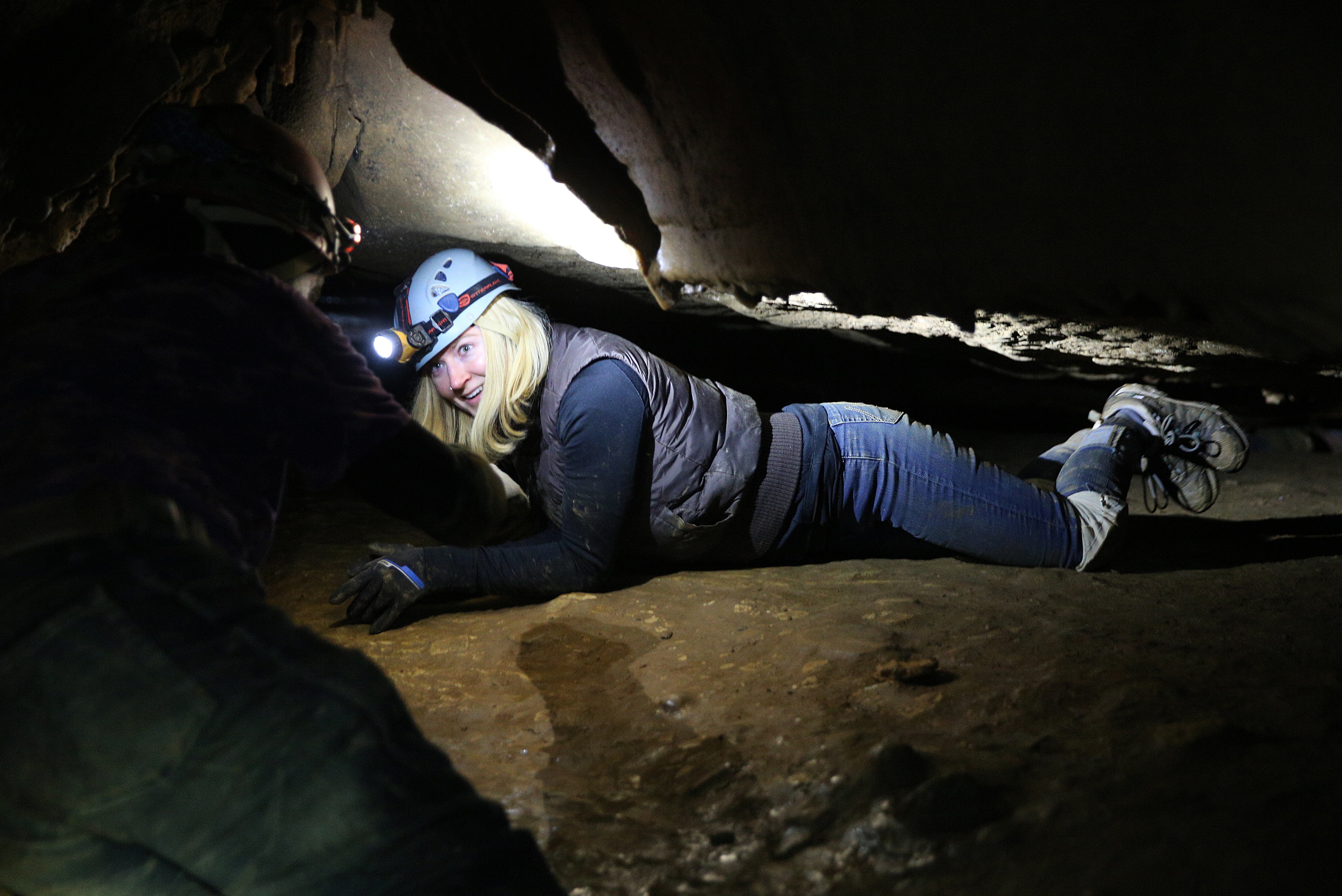 Adventure leader Jerry Wallace coaches a nervous Sunny Montgomery as she climbs on her stomach through a foot-wide section of the cave.