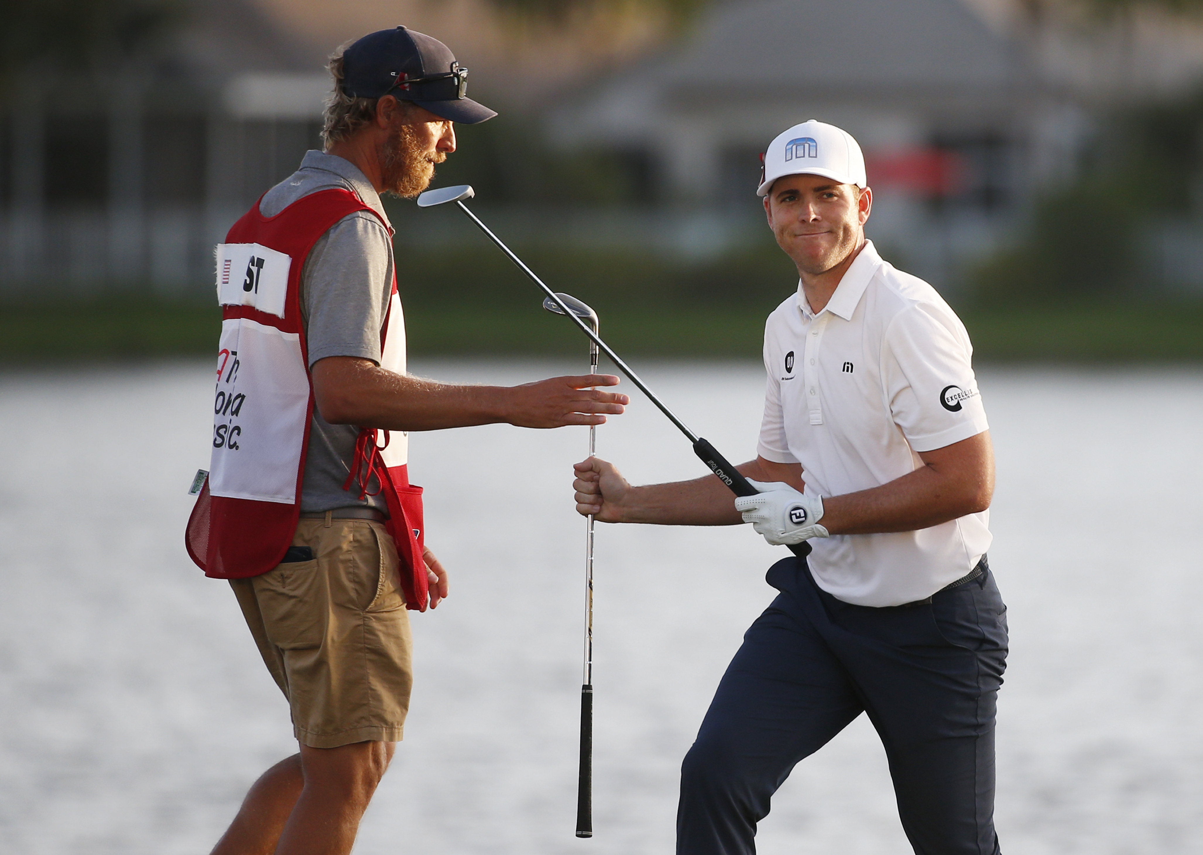 Luke List, right, smiles as he hands his caddie Matt Tritton a club after hitting out of a bunker on the 18th hole during the third round of the Honda Classic golf tournament, Saturday, Feb. 24, 2018 in Palm Beach Gardens, Fla. (AP Photo/Wilfredo Lee)