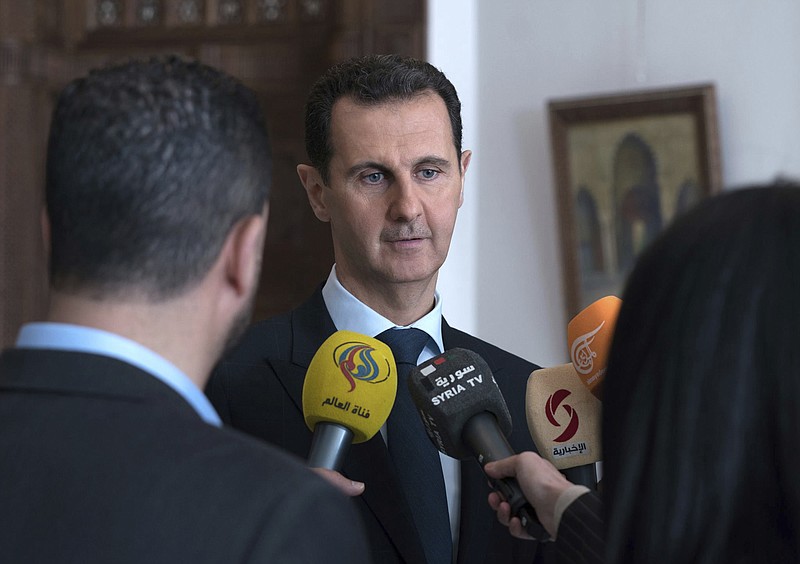 This photo provided by the official Facebook page of the Syrian Presidency, Syrian President Bashar Assad, center, speaks with reporters, in Damascus, Syria, Sunday, March 4, 2018 . Assad vowed Sunday to continue with a military offensive in a rebel-held region near the capital, as troops and allied militias captured a number of villages and towns in the besieged region, in their largest advance since a wide-scale operation began last month. (Syrian Presidency Facebook Page via AP)
