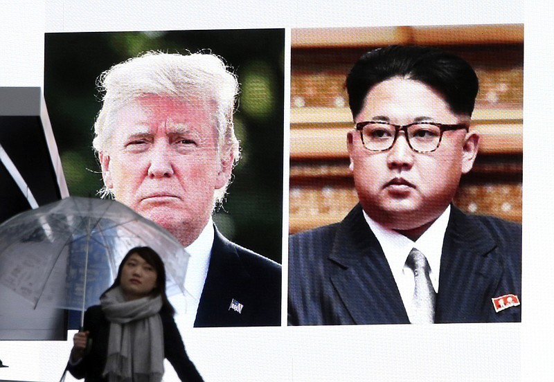 A woman walks by a huge screen showing U.S. President Donald Trump, left, and North Korea's leader Kim Jong Un, in Tokyo, Friday, March 9, 2018. 