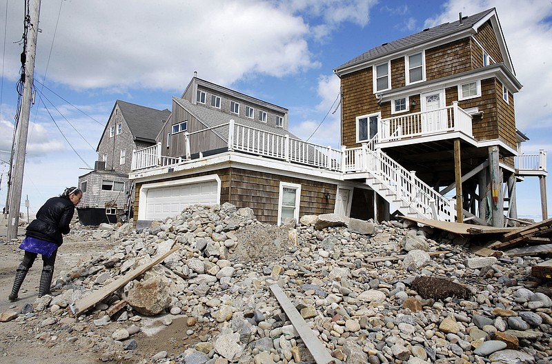 A passerby pauses near a pile of rocks, sand and debris near beachfront homes, Sunday, March 11, 2018, in Marshfield, Mass. The Northeast is bracing for its third nor'easter in fewer than two weeks. The National Weather Service reports Sunday that a southern storm is expected to make its way up the coast causing more snowfall. (AP Photo/Steven Senne)