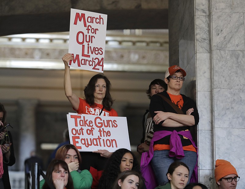 An attendee at a rally against gun violence holds signs that read "March for Our Lives March 24" and "Take Guns Out of the Equation," Tuesday, March 6, 2018, at the Capitol in Olympia, Wash. The rally was held on the same day Gov. Inslee was scheduled to sign a bill banning the sale and possession of gun bump stocks in the state of Washington. (AP Photo/Ted S. Warren)