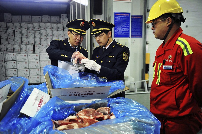 In this April 13, 2017, photo, a warehouse worker watches as government inspectors check imported frozen pork in Qingdao in eastern China's Shandong province. China announced a list of U.S. goods including pork, apples and steel pipe on Friday, March 23, 2018, that it said may be hit with higher import duties in response to President Donald Trump's tariff hike on steel and aluminum. (Chinatopix via AP)