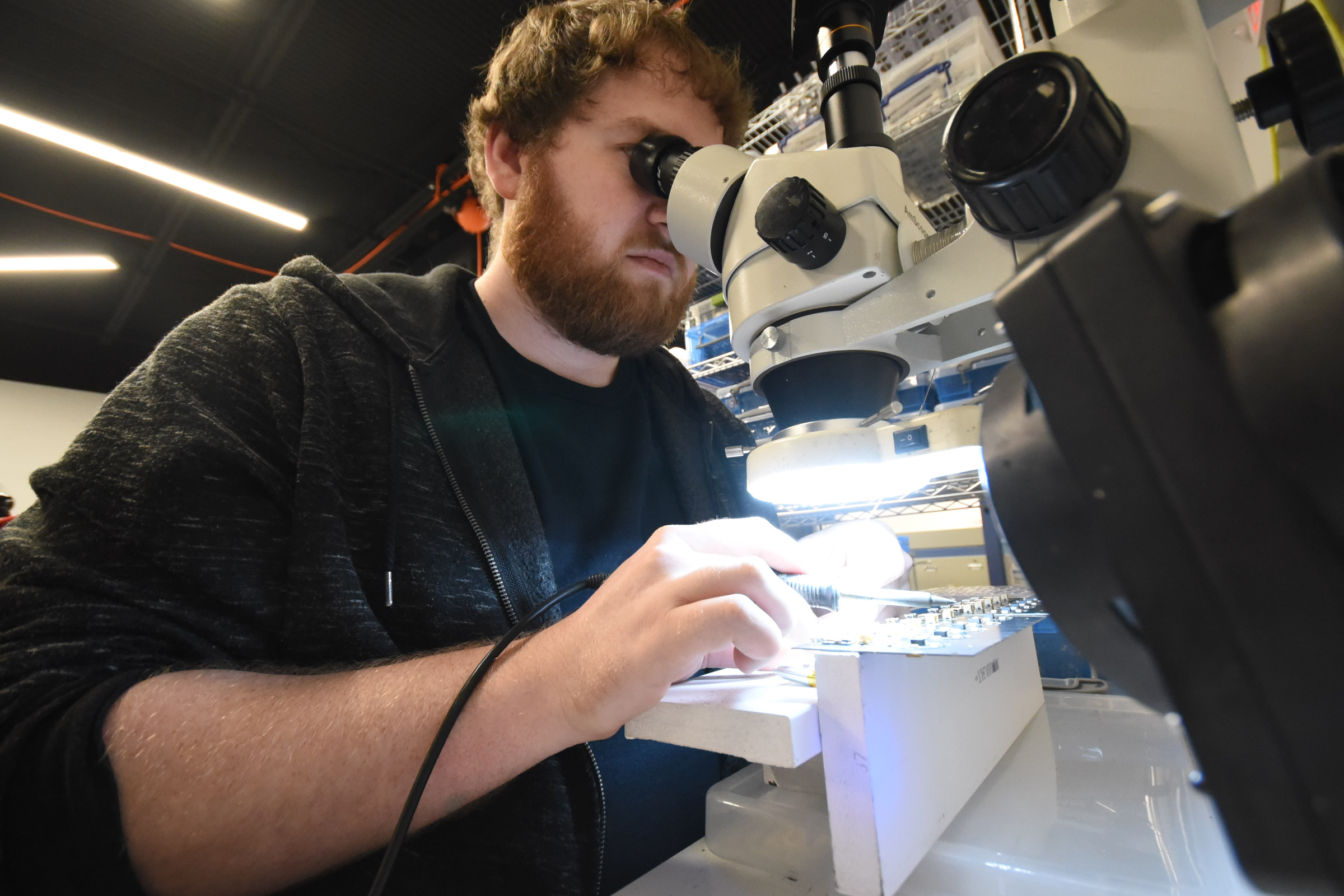Brendon Schafer uses a magnifying eyepiece to solder batteries into a Color Muse device.
