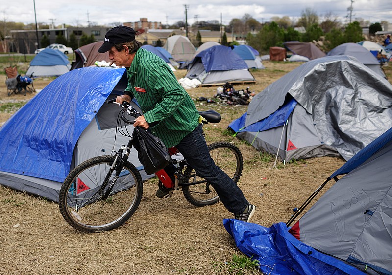 Staff photo by Doug Strickland / Chuck Harris climbs onto his bicycle outside of his tent in a homeless encampment off of East 11th Street last week. More than 100 people are now living on the city-owned lot behind the municipal wellness center, but officials are making them move because the land is a toxic brownfield.