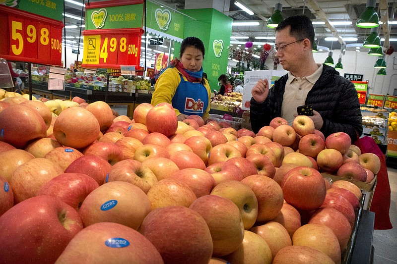 FILE - In this March 23, 2018, file photo, a woman wearing a uniform with the logo of an American produce company helps a customer shop for apples a supermarket in Beijing. China raised import duties on a $3 billion list of U.S. pork, fruit and other products Monday, April 2, 2018 in an escalating tariff dispute with President Donald Trump that companies worry might depress global commerce. (AP Photo/Mark Schiefelbein, FILE)