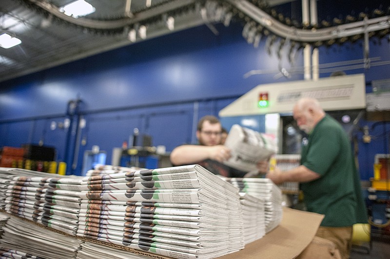 In this April 11, 2018, photo, production workers stack newspapers onto a cart at the Janesville Gazette Printing & Distribution plant in Janesville, Wis. Newspaper publishers across the U.S. already strapped by years of declining revenue say they're dealing with an existential threat: Recently imposed tariffs on Canadian newsprint driving up their business costs. (Angela Major/The Janesville Gazette via AP)