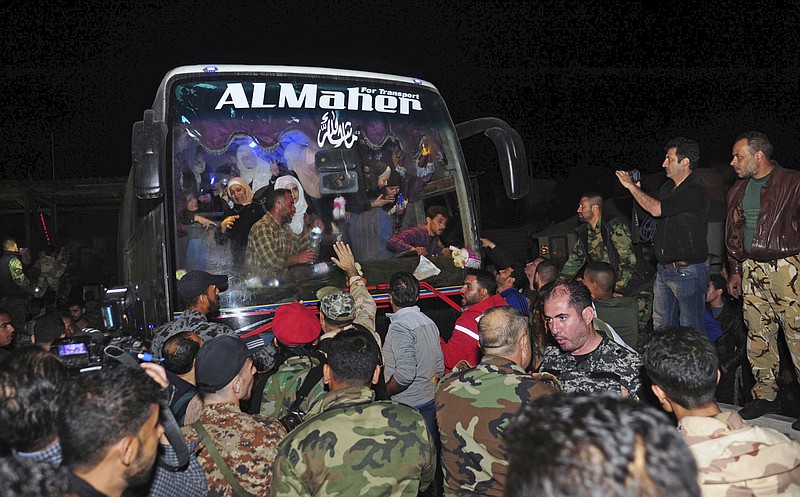 In this photo released by the Syrian official news agency SANA, soldiers and residents salute civilians after they were released by the Army of Islam group that had held them since 2013, in Damascus, Syria, early Monday, April 9, 2018. Syrian state media is reporting that dozens of civilians who had been held for years by a rebel group near the capital Damascus have been freed. (SANA via AP)