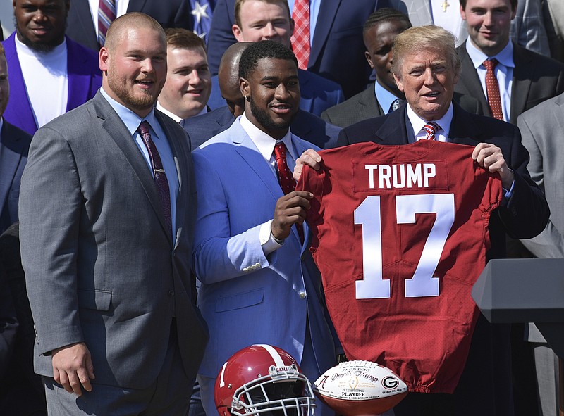 President Donald Trump, right, holds up a jersey he was presented with by Alabama team captains Bradley Bozeman, left, and Rashaan Evans, center, during an event for the 2017 NCAA National Champion University of Alabama football team on the South Lawn of the White House in Washington, Tuesday, April 10, 2018. (AP Photo/Susan Walsh)