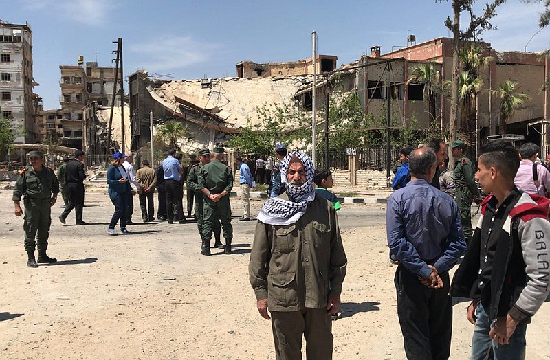 Policemen and civilians stand in front of damaged buildings in the town of Douma, the site of a suspected chemical weapons attack, near Damascus, Syria, Monday, April 16, 2018. Faisal Mekdad, Syria's deputy foreign minister, said on Monday that his country is "fully ready" to cooperate with the fact-finding mission from the Organization for the Prohibition of Chemical Weapons that's in Syria to investigate the alleged chemical attack that triggered U.S.-led airstrikes. (AP Photo/Hassan Ammar)