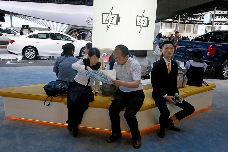 FILE - In this April 19, 2017, file photo, visitors to the stands of GM brands Chevrolet and Buick seat near a section promoting electric power during Auto Shanghai 2017 show at the National Exhibition and Convention Center in Shanghai, China. China has announced plans to allow full foreign ownership of automakers in five years, ending restrictions that have strained relations with Washington and other trading partners. (AP Photo/Ng Han Guan, File)