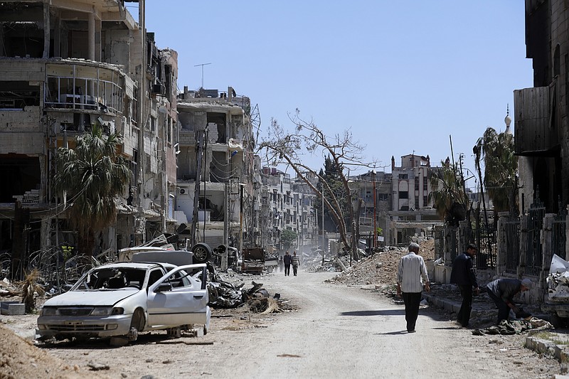 Syrians walk through destruction in the town of Douma, the site of a suspected chemical weapons attack, near Damascus, Syria, Monday, April 16, 2018. Faisal Mekdad, Syria's deputy foreign minister, said on Monday that his country is "fully ready" to cooperate with the fact-finding mission from the Organization for the Prohibition of Chemical Weapons that's in Syria to investigate the alleged chemical attack that triggered U.S.-led airstrikes. (AP Photo/Hassan Ammar)