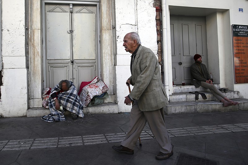 
              An elderly man passes by homeless men in Athens, Monday, April 23, 2018. Greece has beaten its bailout budget targets for a third successive year and eased its massive debt burden by a fraction as the country prepares to exit its international rescue program in four months. (AP Photo/Thanassis Stavrakis)
            