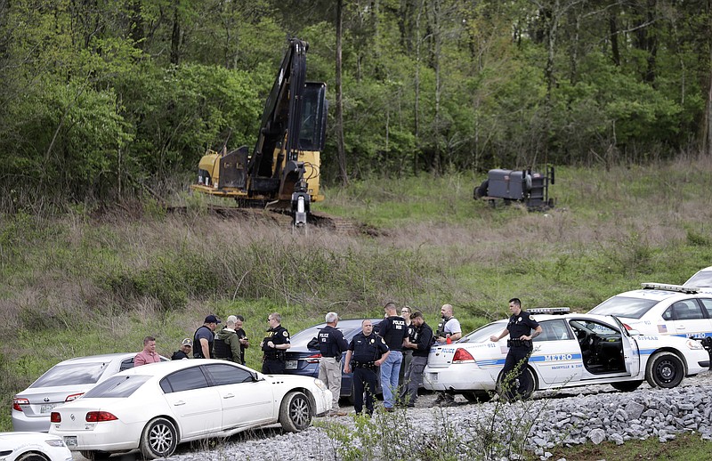 Police gather on a road next to construction equipment in a wooded area near where Waffle House shooting suspect Travis Reinking was captured, Monday, April 23, 2018, in Nashville, Tenn. Police say Reinking shot and killed at least four people at the nearby restaurant in Nashville the day before. (AP Photo/Mark Humphrey)