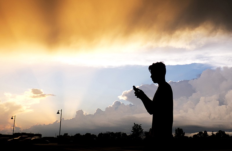 FILE- In this July 17, 2015, file photo, a teenager checks his cell phone as storm clouds pass in Zionsville, Ind. 