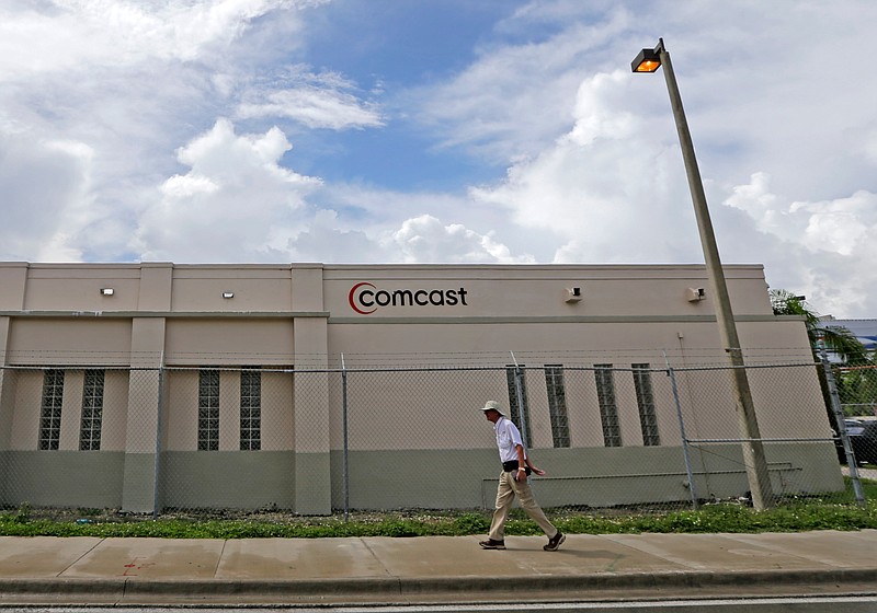 FILE- In this Oct. 12, 2017, file photo a pedestrian walks by a Comcast Service Center, in Miami. Comcast Corp. reports earnings Wednesday, April 25, 2018. (AP Photo/Alan Diaz, File)