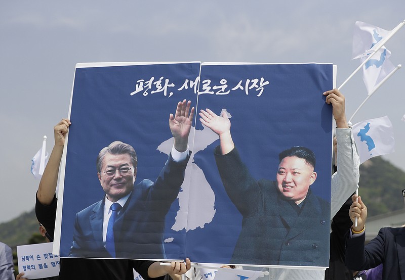 South Koreans hold a banner showing the pictures of South Korean President Moon Jae-in, left, and North Korean leader Kim Jong Un to welcome the planned summit between South and North Koreas near the presidential Blue House in Seoul, South Korea, Thursday, April 26, 2018. Seoul says North Korean leader Kim Jong Un and South Korean President Moon-Jae-in will plant a tree together and inspect an honor guard after Kim walks across the border for the leaders' historic summit. The letters read " Peace, A New Start." (AP Photo/Lee Jin-man)