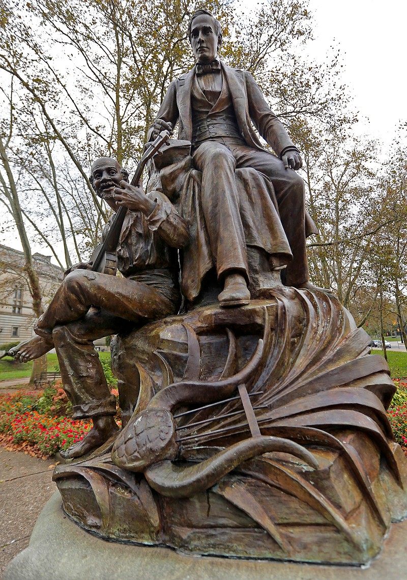 
              FILE – This Oct. 26, 2017, file photo, shows a bronze sculpture of 19th-century songwriter Stephen Foster, top, by Giuseppe Moretti, near the entrance to Carnegie Music Hall in Schenley Plaza in the Oakland neighborhood of Pittsburgh. Workers removed the 118-year-old statue of the "Oh! Susanna" songwriter from the Pittsburgh park Thursday, April 26, 2018, in response to criticism the work is demeaning because it includes a slave sitting at the composer's feet, plucking a banjo. The Pittsburgh Art Commission voted unanimously Oct. 25, 2017, to relocate the statue. (AP Photo/Keith Srakocic, File)
            