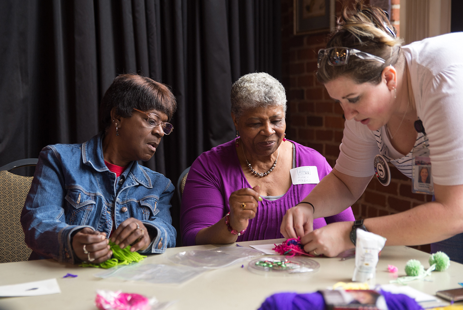 Christina Clark (right) helps Mary Myers and Annie Love make tasseled bag charms.