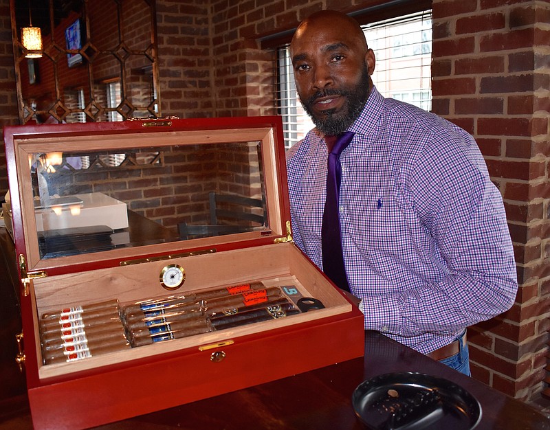 Curtis Greene poses with the tabletop humidor currently stocked at the Chattanooga Cigar Club in downtown. Greene, part-owner of the new lounge and bar, said he will increase the supply of cigars for purchase in the coming weeks once he learns what customers are interested in. (Staff photo by Allison Shirk)