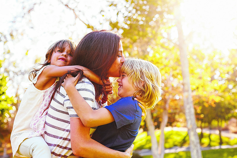 Mother Carrying Son And Daughter As They Play In Park