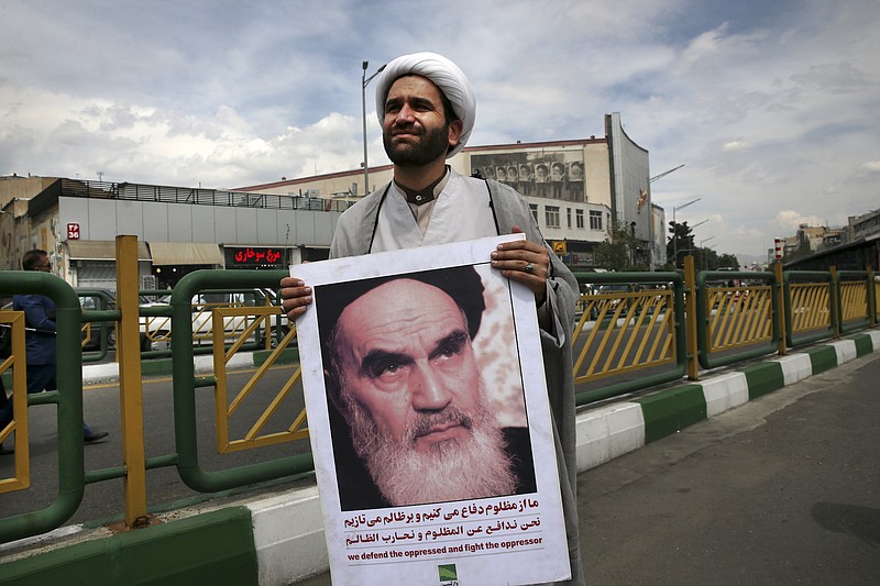 A cleric holds a poster showing portrait of the late Iranian revolutionary founder Ayatollah Khomeini at the conclusion of an anti-U.S. gathering in Tehran, Iran, on Friday. Thousands of Iranians took to the streets in cities across the country to protest U.S. President Donald Trump's decision to pull out of the nuclear deal with world powers. (AP Photo/Vahid Salemi)