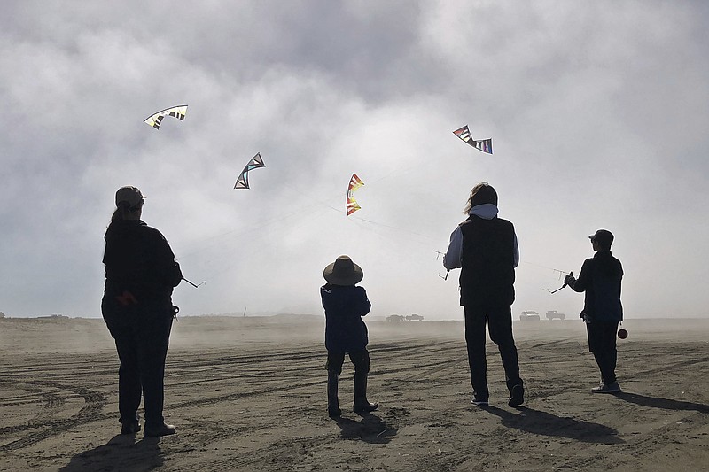 In this March 12, 2018 photo provided by P.V. Nguyen, Dylan Nguyen, from right, Scott Weider, Cardin Nguyen and Linda Marsland are shown flying kites in the fog at Long Beach, Wash. (P.V. Nguyen via AP)