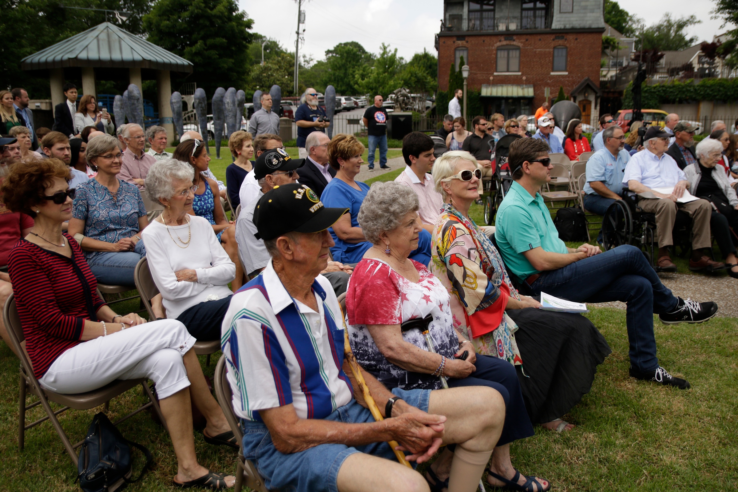 People listen to a speaker during the Veterans Bridge Flag Raising Ceremony in the Bluff View Sculpture Garden on Friday, May 18, 2018, in Chattanooga, Tenn. The annual installation of new American flags on the bridge ahead of Armed Forces Day honors the city's veterans.