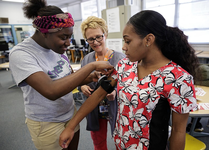Health sciences teacher Tina Lutz, center, watches Tychicia Driver, left, practice putting a tourniquet on classmate Darianna King during a "Stop the Bleed" class at Brainerd High School on April 11 in Chattanooga, Tenn. Erlanger provided first aid training focused on slowing blood loss in trauma victims for the health occupations classes and interested faculty and students at Brainerd.