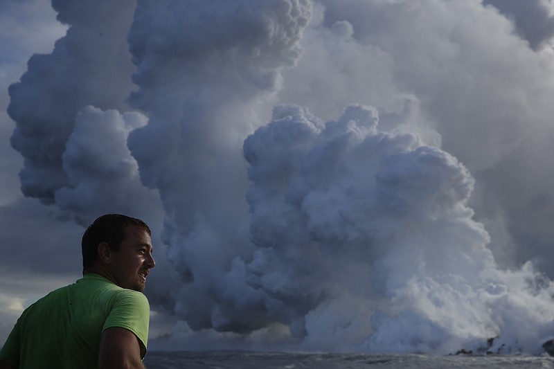 Joe Kekedi watches as lava enters the ocean, generating plumes of steam near Pahoa, Hawaii Sunday, May 20, 2018. Kilauea volcano that is oozing, spewing and exploding on Hawaii's Big Island has gotten more hazardous in recent days, with rivers of molten rock pouring into the ocean Sunday and flying lava causing the first major injury. (AP Photo/Jae C. Hong)