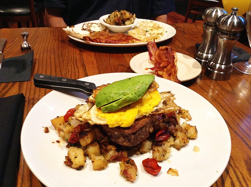 Steak & Eggs, foreground, from Bluewater Grille's brunch menu features a 10-ounce, center-cut filet topped with two fried eggs and served with garlic cherry tomatoes, sliced avocado and brunch potatoes. In back are a la carte menu items Canadian bacon, English muffin, brunch potatoes and eggs.