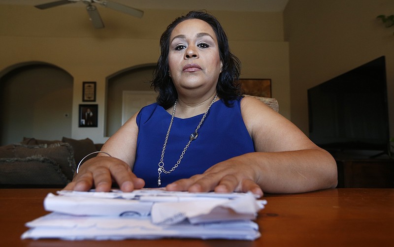 In this April 13, 2018, photo Josephine Rizo sits in her home with her stack of bills from her ongoing battle with cancer in Phoenix.