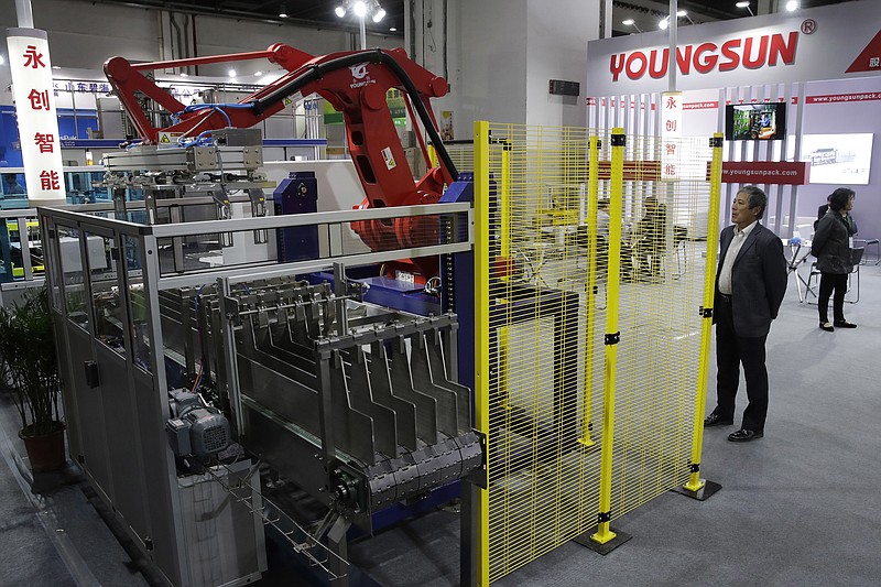 In this April 12, 2018, photo, a visitor watches a Chinese company displaying a Chinese-made industrial robot demonstration on processing soybean at the International soybean exhibition in Shanghai. China says it will narrow its trade surplus with the United States but rejects pressure to change technology development tactics seen as a path to prosperity and its rightful place as a global leader. Beijing highlighted the sensitivity of the issue with its threat to scrap deals aimed at settling a sprawling trade dispute with Washington if President Donald Trump's threatened tariff hike on $50 billion of Chinese technology goes ahead. (AP Photo/Andy Wong)