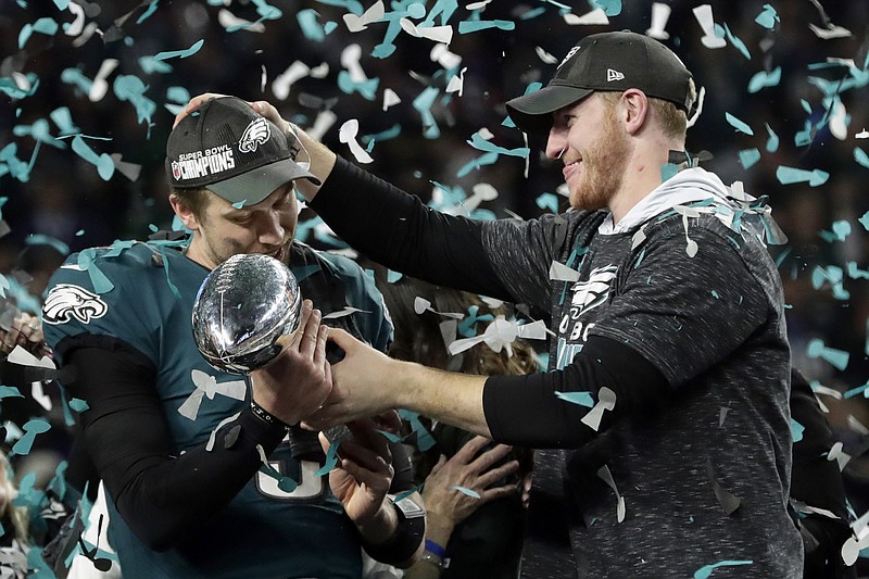 In this Feb. 4, 2018 photo, Philadelphia Eagles quarterback Carson Wentz, right, hands the Vincent Lombardi trophy to Nick Foles after winning the NFL Super Bowl 52 football game against the New England Patriots in Minneapolis. The Eagles won 41-33. President Donald Trump has called off a visit by the Philadelphia Eagles to the White House Tuesday due to the dispute over whether NFL players must stand during the playing of the national anthem. Trump says in a statement that some members of the Super Bowl championship team "disagree with their President because he insists that they proudly stand for the National Anthem, hand on heart." Trump says the team wanted to send a smaller delegation, but fans who planned to attend "deserve better." (AP Photo/Frank Franklin II)