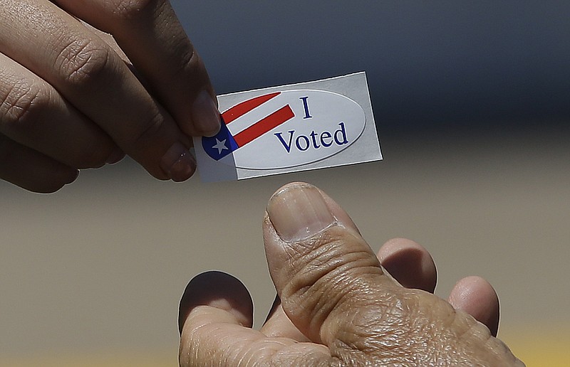 Kimberlee Weaver, left, an election worker for the Sacramento County Registrar of Voters, hands an "I Voted" sticker to a voter during the state's primary elections, Tuesday, June 5, 2018, in Sacramento, Calif. (AP Photo/Rich Pedroncelli)