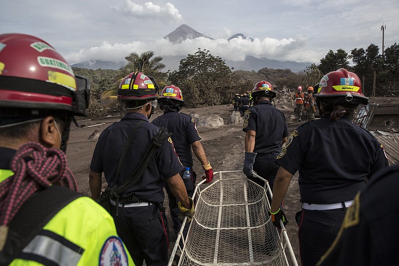 Volcan de Fuego, or "Volcano of Fire," releases a white plume of smoke as firefighters carry a stretcher during their rescue and  recovery efforts in El Rodeo, Guatemala, Wednesday, June 6, 2018. Rescuers were concerned about possible dangers posed not only by more volcanic flows but also rain. Authorities have said the window is closing on the chances of finding anyone else alive in the devastation. (AP Photo/Rodrigo Abd)