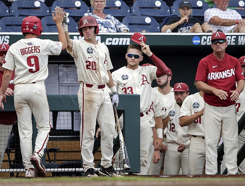 Arkansas shortstop Jax Biggers is greeted at the dugout by teammate Carson Shaddy (20) after Biggers scored against Texas on a base hit by Heston Kjerstad in the sixth inning of Sunday's 11-5 win against Texas at the College World Series in Omaha, Neb.