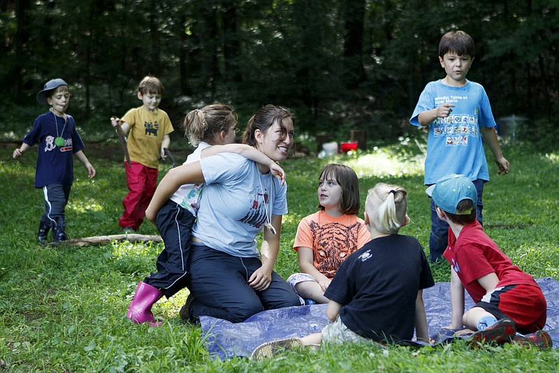 As 4-year-old Zoe climbs on her back, counselor Rosie Garber gathers the students around after free play during a German language immersion camp, part of the Wauhatchie's Forest School School Summer Camp, at Reflection Riding Arboretum and Nature Center on Friday, June 22, 2018 in Chattanooga, Tenn.