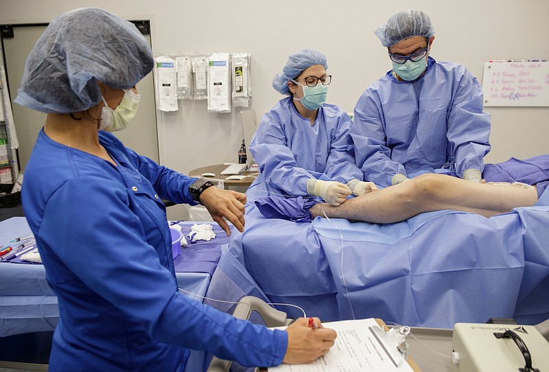 Nurse Christine Warren, left, counts out time as Dr. Chris Lesar, right, and radiology technologist Erin Wehunt perform an endovenous laser therapy procedure at the Vascular Institute of Chattanooga on Friday, June 15, 2018, in Chattanooga, Tenn. VIC is among a handful of medical practices in the country using cutting-edge technology to treat peripheral artery disease and critical limb ischemia with a focus on preventing amputations.